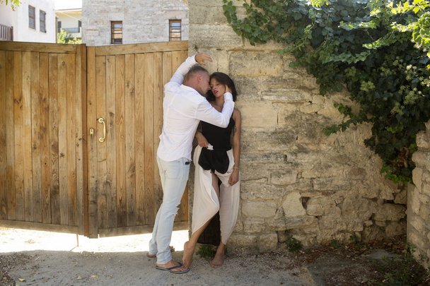 Sensual couple hiding out of sun with ancient rocky wall and old fence on background. Couple in love hugs in shadow on hot sunny summer day. Man and woman full of desire. Hot and desire concept. - Φωτογραφία, εικόνα