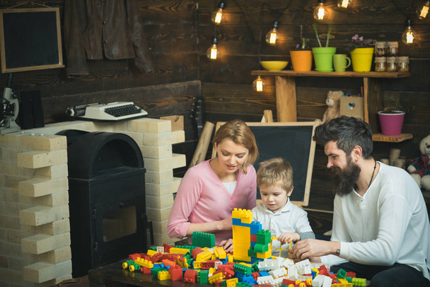 Family spend time together in playroom. Kid with parents play with plastic blocks. Father, mother and cute son play with constructor bricks. - Foto, afbeelding