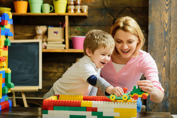Motherhood concept. Blond mom and son play with plastic building blocks train. Excited preschooler playing with his smiling mother or kindergarten teacher. - Photo, Image