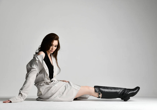Beautiful brunette hipster woman in gray autumn jacket coat and black leather boots shoes sitting on grey  - Photo, Image