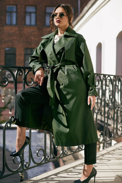Beautiful elegant brunette woman wearing green coat on the balcony - Фото, изображение