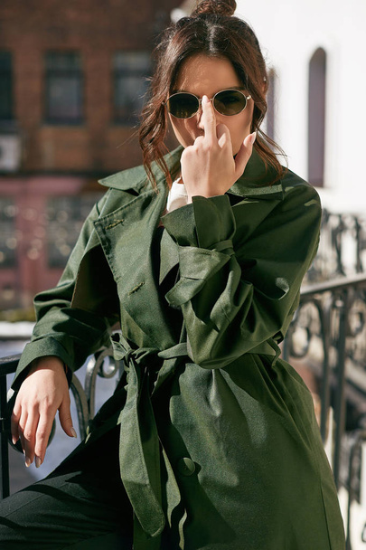 バルコニーの緑のコートを着てエレガントなブルネット美人 - 写真・画像