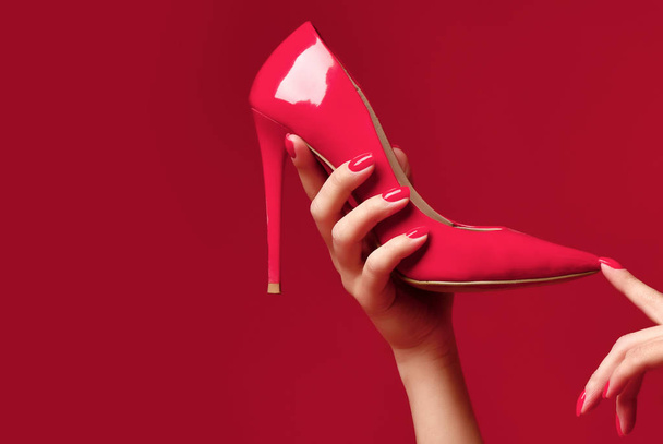 Woman hands hold red high hill shoe on dark pink red  - Foto, Imagem