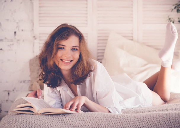 lifestyle and people concept: blond woman lying in bed while reading a book - Valokuva, kuva