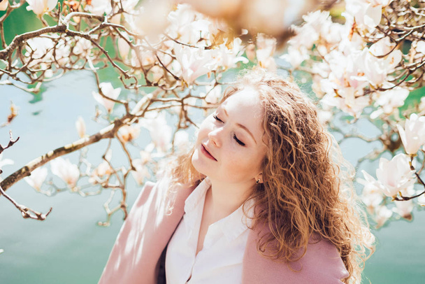an attractive curly-haired woman walks through the spring garden, enjoys the scent of flowering trees - Foto, Bild