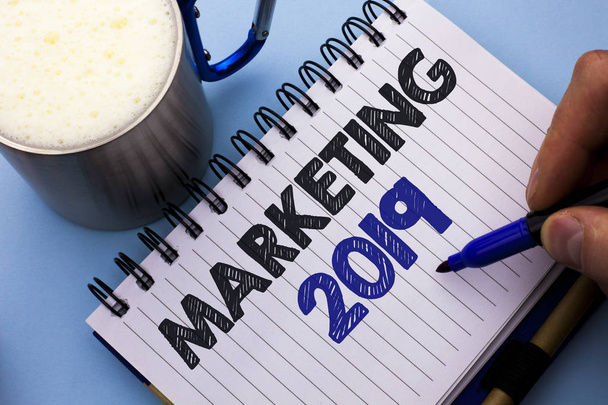Conceptual hand writing showing Marketing 2019. Business photo text New Year Market Strategies Fresh start Advertising Ideas written by Man on Notebook Book Holding Marker plain background Cup. - Photo, Image