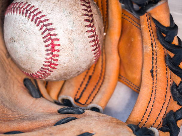 Imagen de fondo deportiva de una vieja pelota de béisbol de cuero envejecida con cordones rojos dentro de un guante o guante de béisbol que muestra detalles intrincados y cordones de cuero negro
. - Foto, imagen
