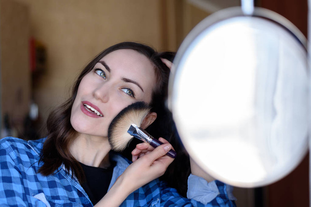 Mujer feliz con maquillaje de cepillo cosmético espejo redondo se aplica al tono de la piel
 - Foto, imagen
