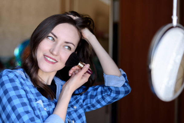 Young brunette corrects make-up at the round mirror in the bedroom - Фото, зображення