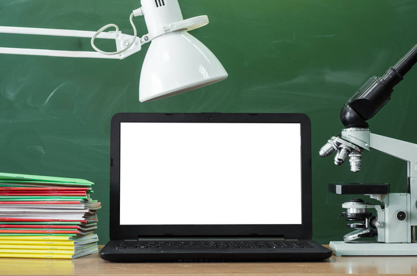 Teacher or student desk table. Education background. Education concept. Laptop with blank screen, microscope and stacked books on the table. - Foto, imagen