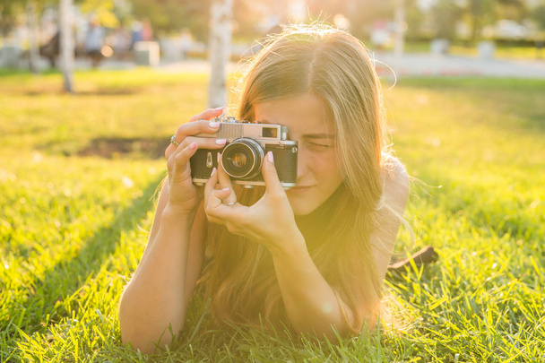 Mujer joven sonriente usando una cámara retro para tomar fotos en el parque
. - Foto, Imagen
