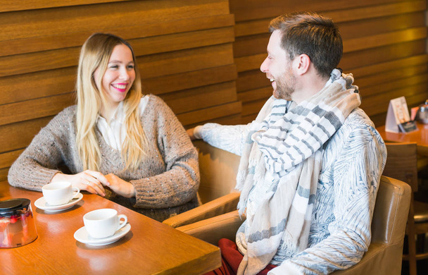 Happy young couple is talking and drinking coffee and smiling while sitting at the cafe. - Photo, Image