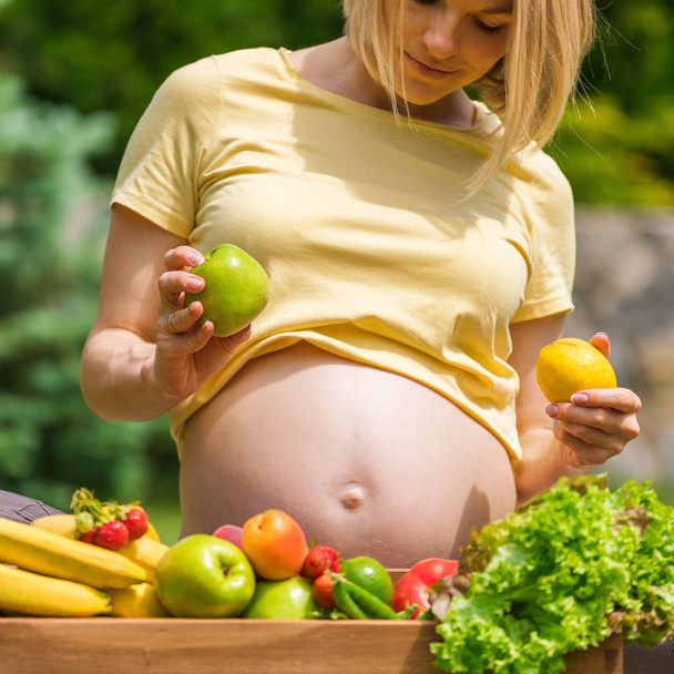Pregnant woman sitting on grass and holding an apple in hand - Foto, Bild