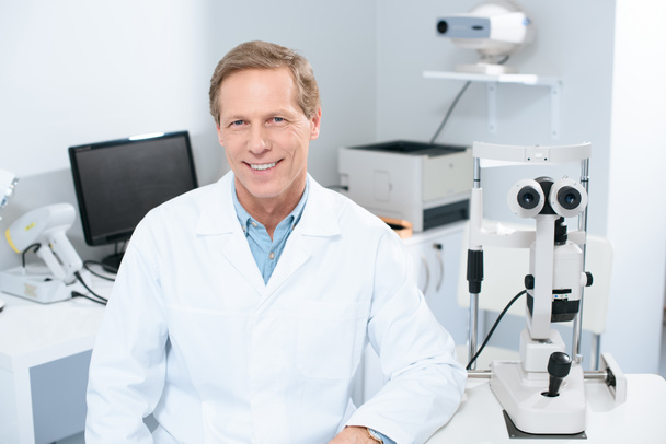 guapo oftalmólogo sonriente mirando a la cámara en la sala de consulta
 - Foto, imagen