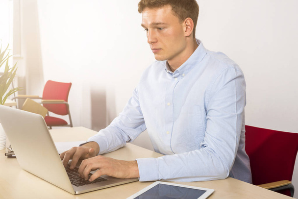 Молодий бізнесмен використовує свій ноутбук, офіс в приміщенні
. - Фото, зображення