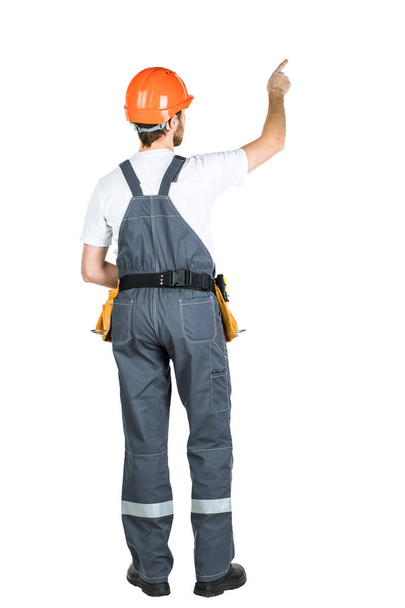 Μια κατασκευή άνθρωπος στέκεται με την πλάτη του και δείχνει το χέρι του. Επισκευή και κατασκευή. Απομονωθεί σε λευκό φόντο - Φωτογραφία, εικόνα