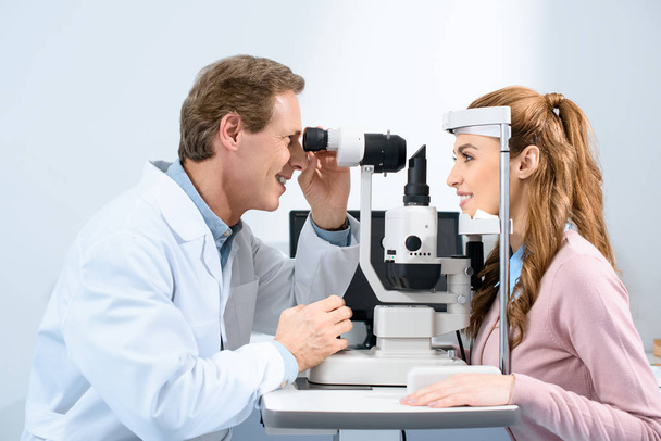 Widok z boku okulista badanie wzroku pacjenta z Lampa w klinice szczelinowa - Zdjęcie, obraz