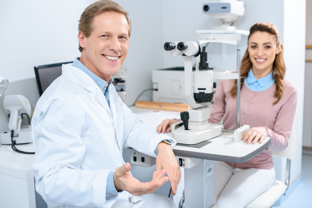 smiling ophthalmologist and patient near slit lamp in clinic - Photo, Image