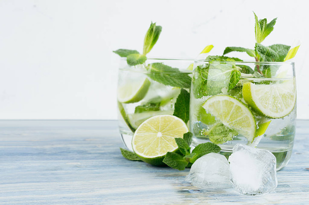 Bevanda fresca estiva gin tonic con lime, menta in foglia, paglia, cubetti di ghiaccio, soda su fondo bianco chiaro
. - Foto, immagini