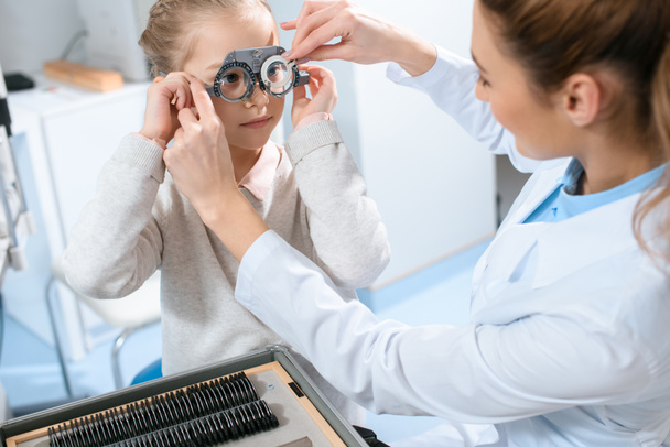 female ophthalmologist examining kid eyes with trial frame and lenses - Photo, Image