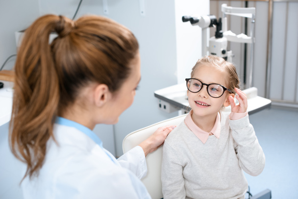 ophthalmologist and smiling kid in eyeglasses in optics  - Фото, изображение