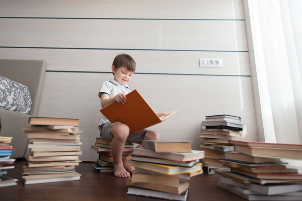 Le garçon est assis sur des livres et lit. Autour de lui se trouvent de nombreux livres colorés
. - Photo, image