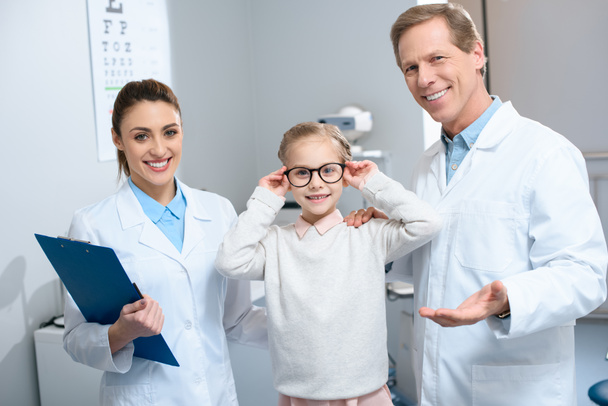 two smiling ophthalmologists and little child in eyeglasses - Fotografie, Obrázek