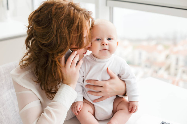 Portrait of business woman sitting and talking on her cellphone while hugging her little cute baby isolated - Photo, Image