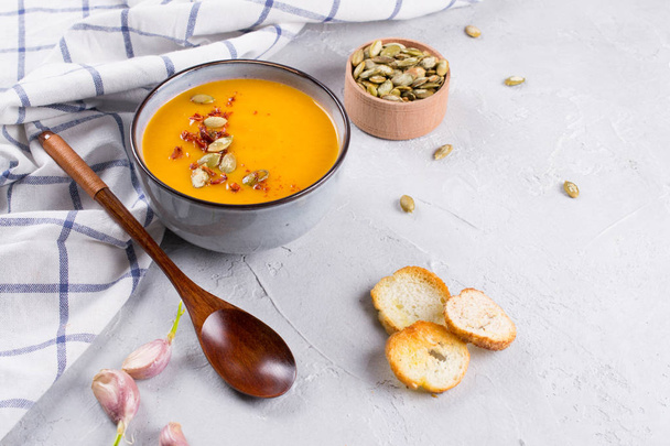 Pumpkin cream soup with seeds, toast and seasoning in a ceramic bowl on a table. Copy space - Photo, Image