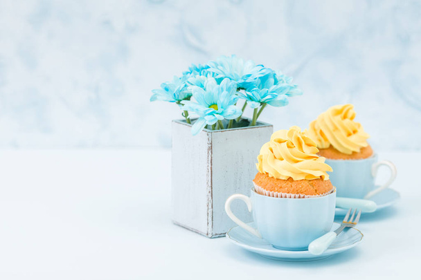 Cupcake con tenera crema gialla decorazione e bouquet di crisantemo blu in vaso shabby chic retrò su sfondo blu pastello
. - Foto, immagini