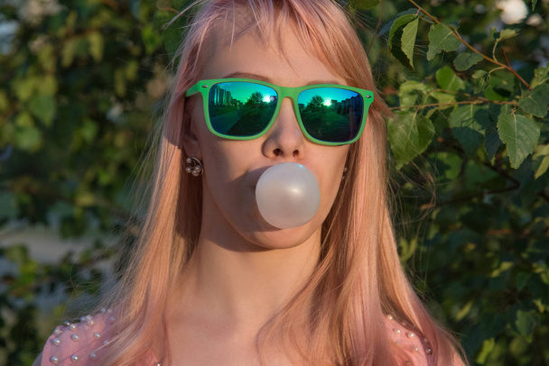 Young girl in green glasses with long hair puffs bubble of chewi - Fotoğraf, Görsel