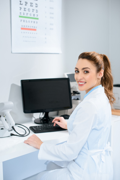 Óptica femenina sonriente trabajando con computadora en la clínica
 - Foto, Imagen