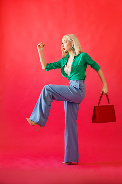 Prachtige Blonde vrouw mannequin met handtas op rood  - Foto, afbeelding