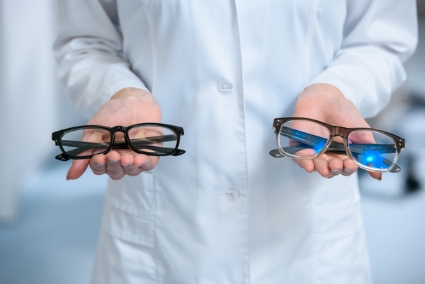 Ausgeschnittene Ansicht des Augenoptikers mit verschiedenen Brillen in der Hand - Foto, Bild