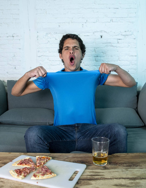 Young football fan celebrating a goal during watching football game on couch. Man watching soccer with beer and pizza - Photo, Image