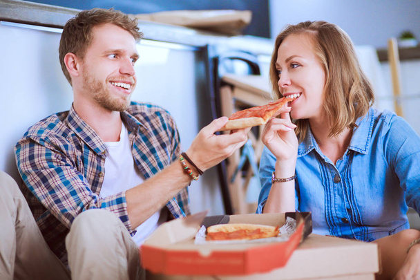 Giovani coppie hanno una pausa pranzo pizza sul pavimento dopo essersi trasferiti in una nuova casa con scatole intorno a loro. Coppia giovane - Foto, immagini