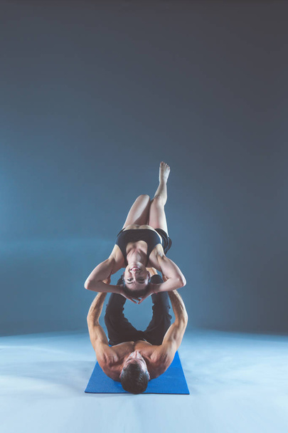 Young couple practicing acro yoga on mat in studio together. Acroyoga. Couple yoga. Partner yoga. - Fotoğraf, Görsel