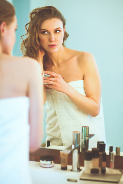 Young woman looking in the mirror and putting make-up on. - Fotografie, Obrázek