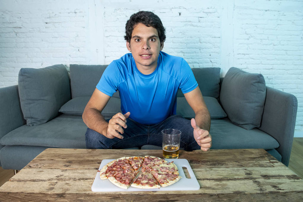 Young football fan disappointing during watching football game on couch. Man watching soccer with beer and pizza - Photo, image