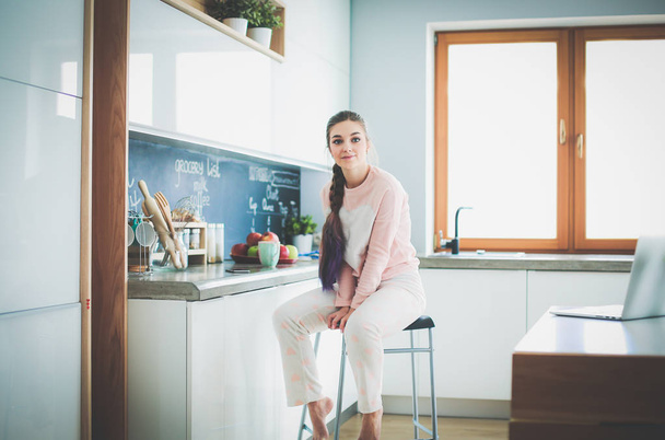 Young woman sitting on table in the kitchen. - Fotografie, Obrázek