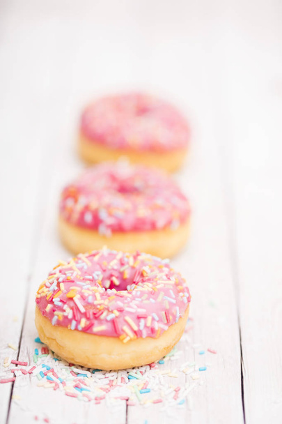 Rosafarbene Donuts mit Funkeln auf Holztisch  - Foto, Bild