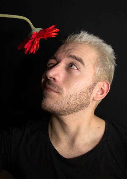 A portrait of a young bearded man. A guy looking up on a red flower. A portrait of a man on a black background. - Φωτογραφία, εικόνα