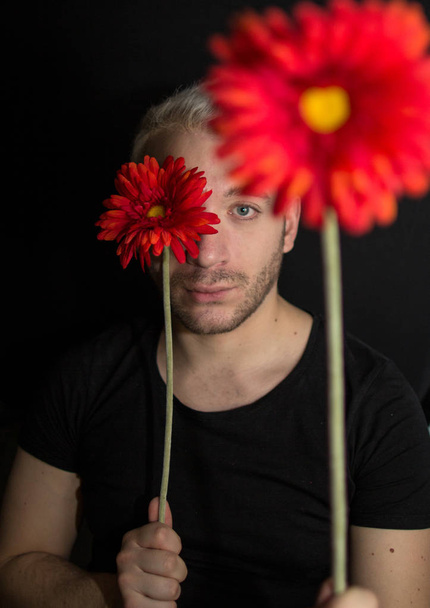 A portrait of a young bearded man with two red flowers on a black background. Portrait of a man looking to camera. - Foto, Imagem