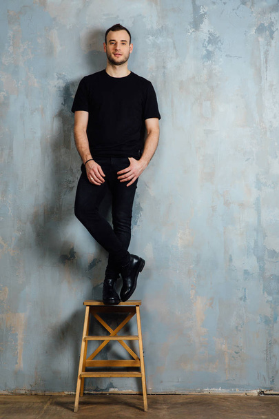 portrait of a young man in a black T-shirt leaned against a vintage gray wall. Copy space. - Foto, Bild