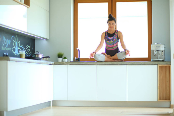 Young beautiful woman sitting at the kitchen table in the lotus position. Woman. Yoga - Фото, зображення