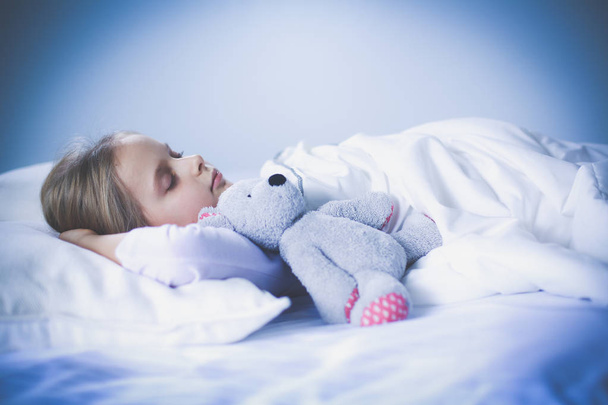 criança menina dorme na cama com um brinquedo ursinho de pelúcia
. - Foto, Imagem