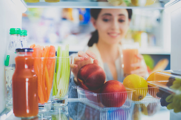 Portrait of female standing near open fridge full of healthy food, vegetables and fruits. Portrait of female - Zdjęcie, obraz