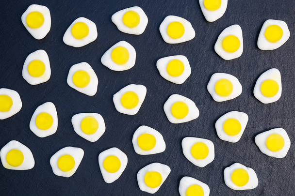Fried eggs candy sweets overhead on dark background - Photo, Image