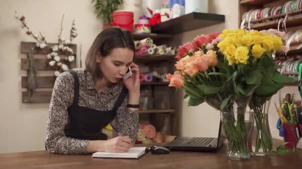 kukkakauppias puhuu puhelimessa, nainen tekee kukkakimpun lomalle
 - Materiaali, video