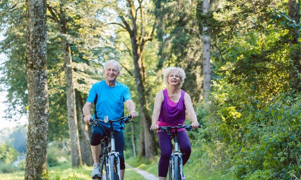 Happy and active senior couple riding bicycles outdoors in the park - Photo, Image